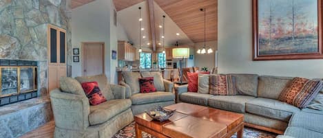 A spacious living room with a stone wall, wooden ceiling beams, and a large painting.