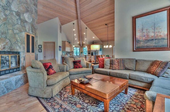 A spacious living room with a stone wall, wooden ceiling beams, and a large painting. - Luxurious home on the golf course (Sunriver)