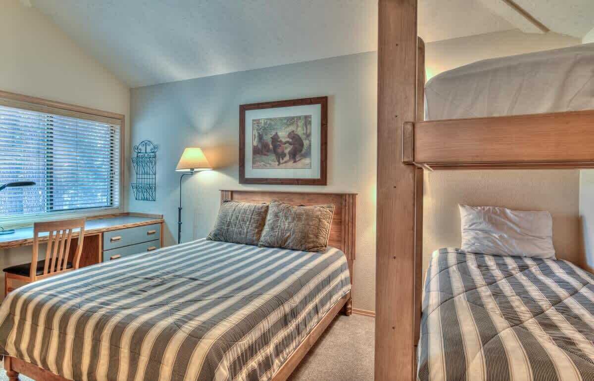 A bedroom with a bed, a desk, and a chair. There is a picture on the wall and a lamp on the desk.