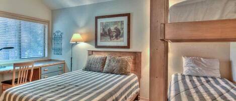 A bedroom with a bed, a desk, and a chair. There is a picture on the wall and a lamp on the desk.