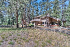 A two-story log cabin with a covered porch and a chimney, surrounded by tall pine trees. - Luxurious home on the golf course (Sunriver)