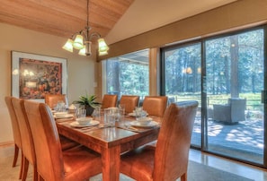 A dining area with a wooden table set for six, surrounded by leather chairs, with a large window offering a view of a forested area.