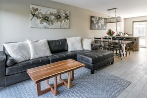 Ein modernes Wohnzimmer mit einer Eckcouch, einem Holztisch und einem gemusterten Teppich.