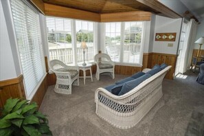 A sunlit room with wicker furniture, a cushioned bench, and a view through large windows. - Beach Equipment - Linens - Keurig - GIANT Community Pool! (Duck)