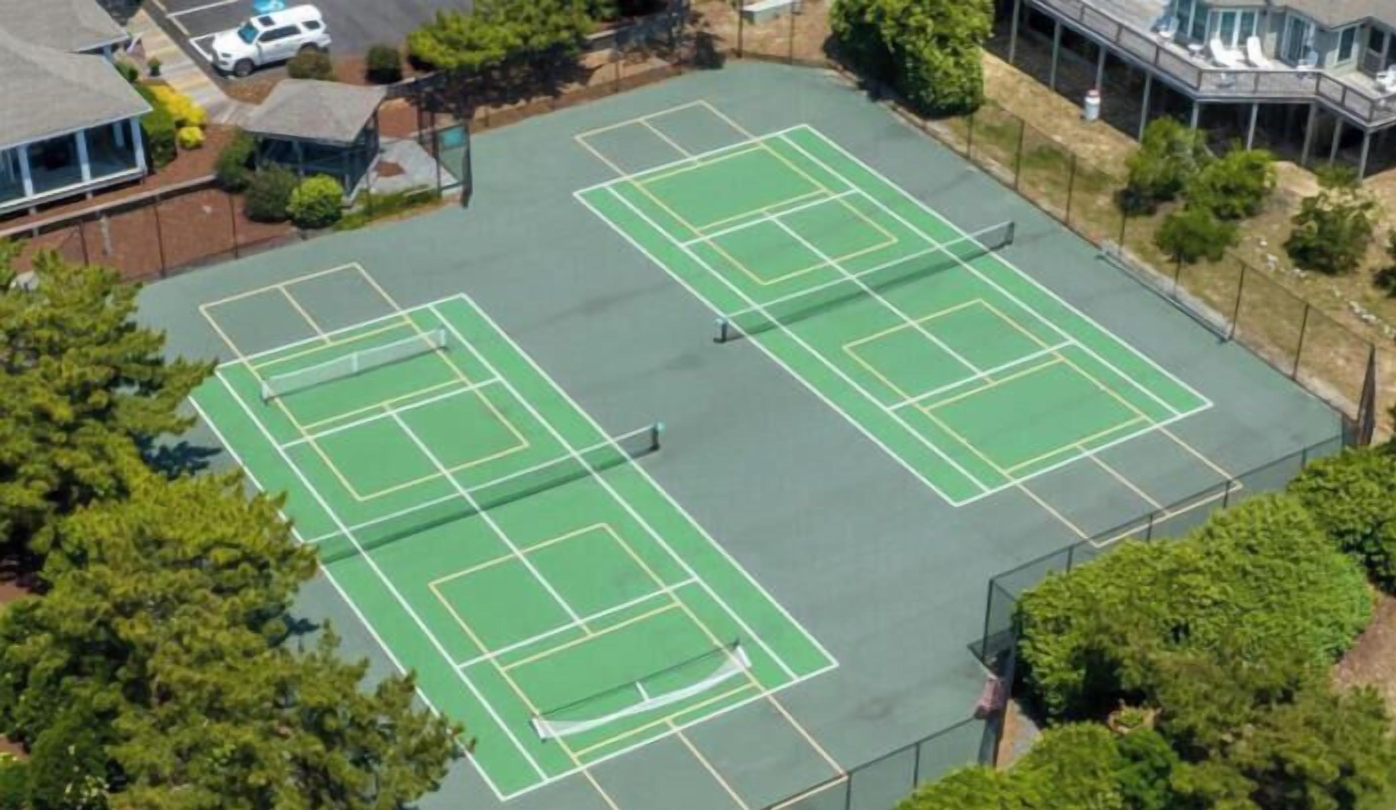 Vue aérienne d’un complexe de courts de tennis comprenant plusieurs terrains, entouré d’arbres et de bâtiments.