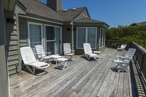 Une terrasse en bois avec des chaises longues blanches disposées autour d’un petit espace abrité doté de fenêtres.