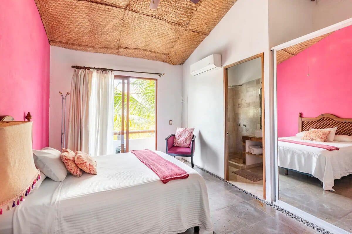 Ein Schlafzimmer mit zwei Betten, einem großen Fenster, einem Sessel und einer Schiebetür zum Badezimmer.
