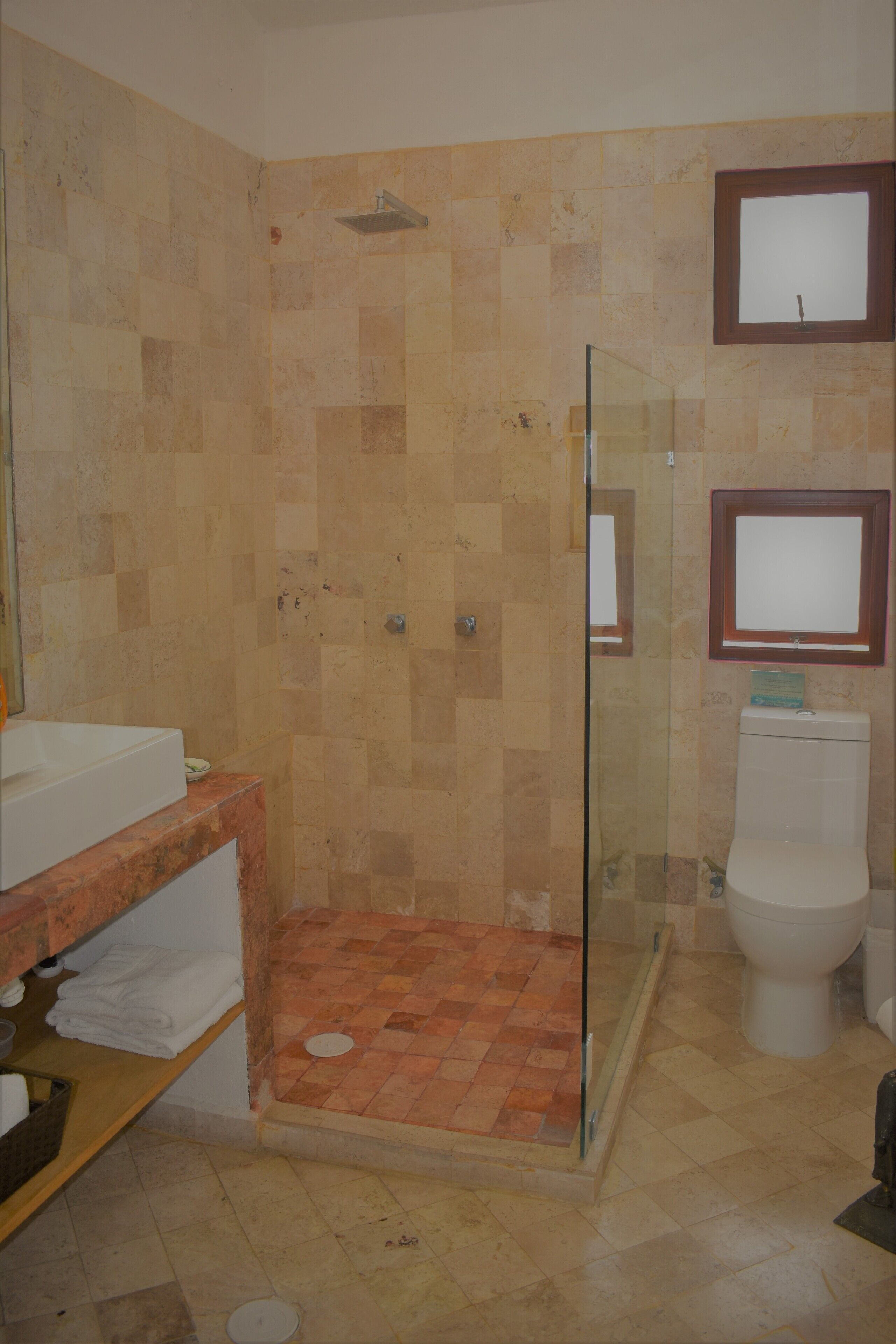 Een badkamer met een douchecabine van glas, een wit toilet en een wastafel met een marmeren aanrecht.
