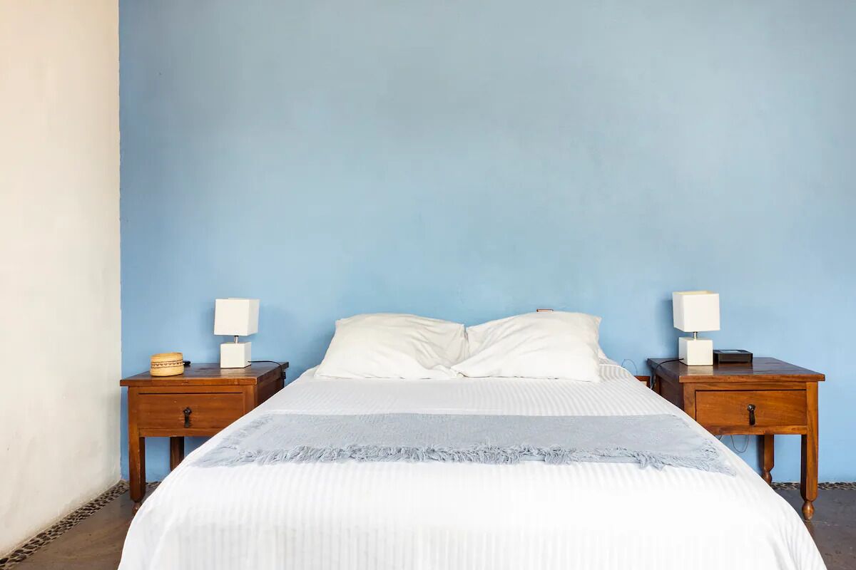 Un dormitorio con una cama, dos mesitas de noche y una pared azul.