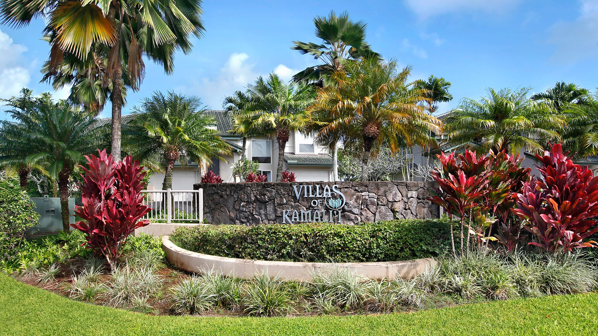 Un jardin bien entretenu, agrémenté d’un mur en pierre et d’une enseigne indiquant « Villas de Kamai’i ».