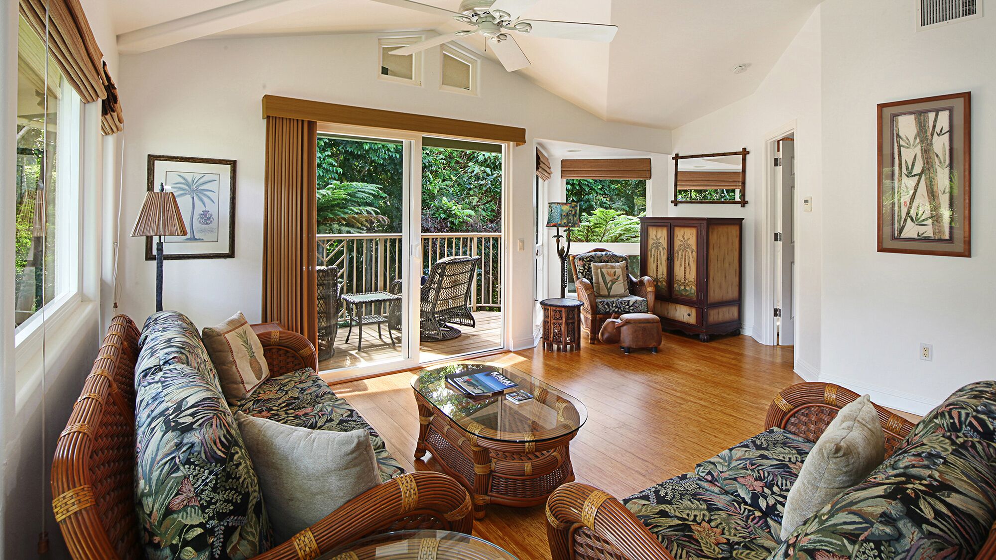 A spacious living room with a large glass door leading to a balcony, wicker furniture, and a ceiling fan.
