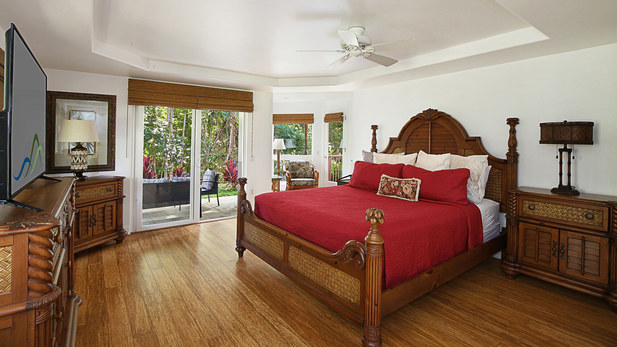 A spacious bedroom with a large bed, wooden furniture, and a view of the outdoors through sliding glass doors.