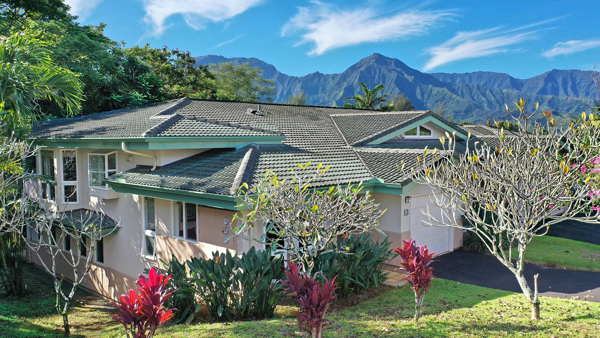A house with a tiled roof, surrounded by lush greenery and mountains in the background.