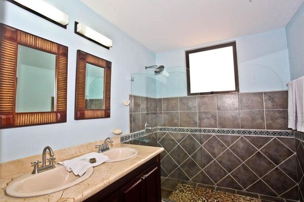 A bathroom with two sinks, a glass shower enclosure, and a small window.