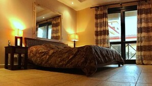 Quarto com cama, mesa de cabeceira, espelho e janela com cortinas.