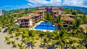 Um resort com piscina central, vários edifícios e palmeiras.