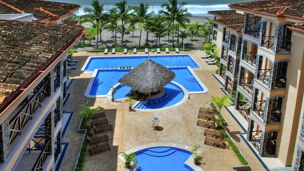 Um resort com várias piscinas, vista para a praia e uma estrutura com telhado de palha.