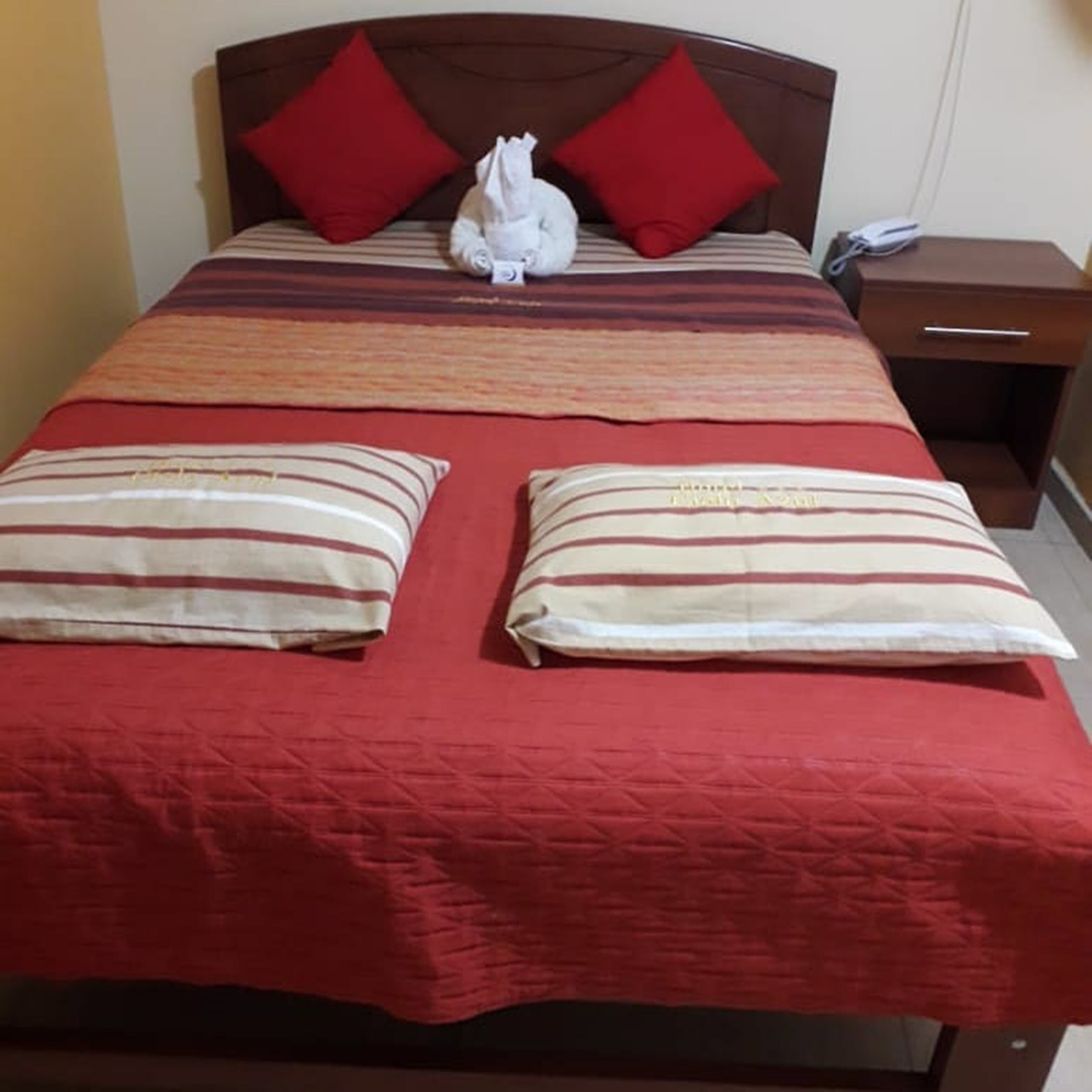 Una cama con una colcha roja, dos almohadas a rayas y dos almohadas rojas.
