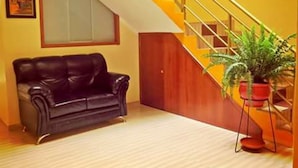 A living room with a black leather sofa, a wooden door, a staircase with yellow railings, and a potted plant. - Hotel Cielo Azul (Cajamarca)