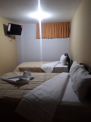 A small, dimly lit room with two beds, a television mounted on the wall, and a window with a curtain. - Hotel Cielo Azul (Cajamarca)