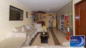 A living room with a beige sofa set, a coffee table with a vase of flowers, and a hallway with a wooden door and a bulletin board. - Hotel Cielo Azul (Cajamarca)