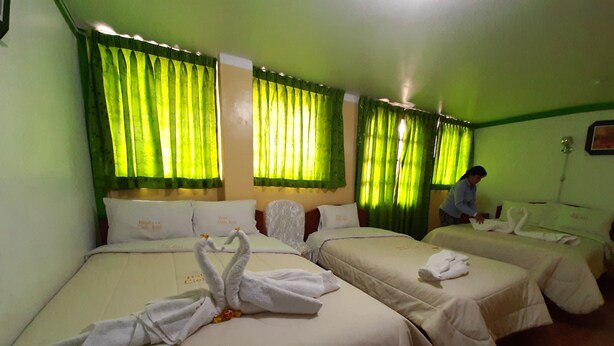 A hotel room with three beds, each with white bedding and decorative swan towels. Green curtains cover the windows, and a person is visible in the room. - Hotel Cielo Azul (Cajamarca)