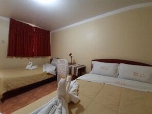 A hotel room with two beds, a red curtain, a small table with a vase of flowers, and a towel rack with towels. - Hotel Cielo Azul (Cajamarca)