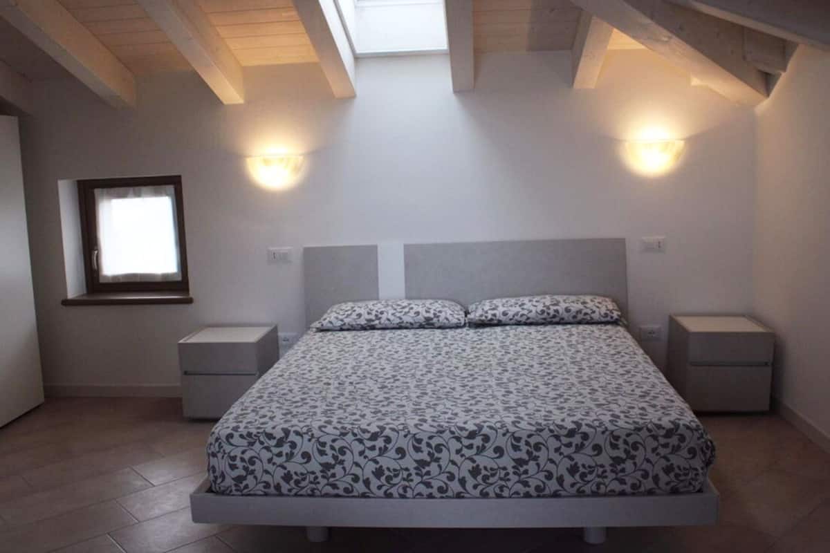 A bedroom with a bed, nightstands, a window, and two wall-mounted lights.