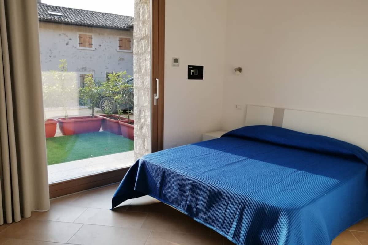 A bedroom with a bed, a sliding glass door leading to a courtyard with a lawn and potted plants.