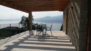 Un espacio al aire libre cubierto con una mesa y sillas, vista a un cuerpo de agua y montañas, y una pared de piedra.