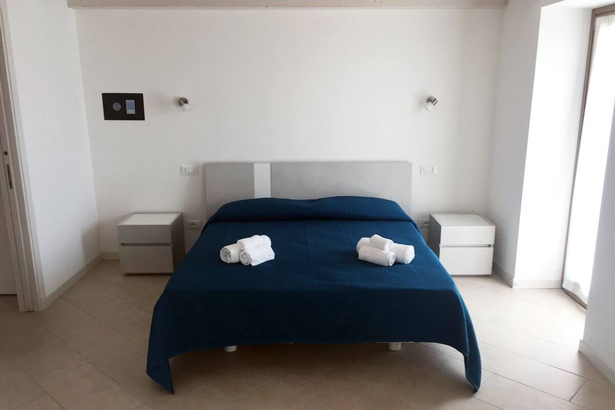 A hotel room with a bed, two bedside tables, and a window.