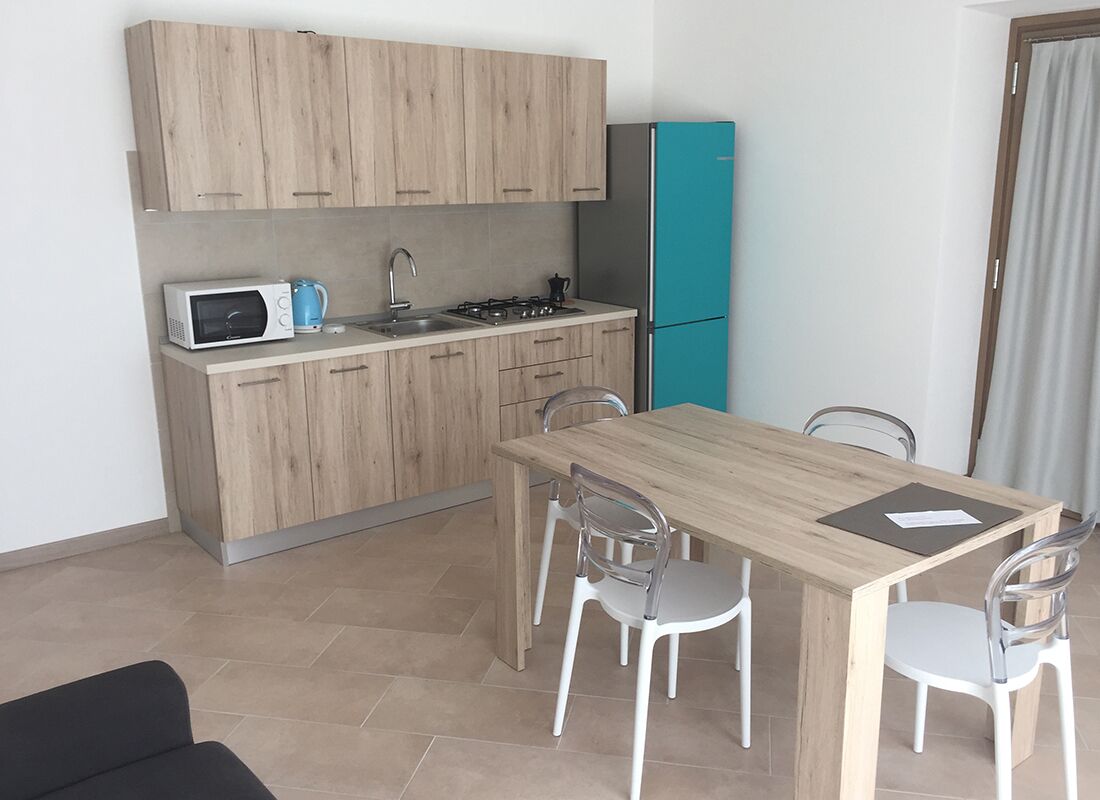 Une cuisine compacte avec des meubles en bois, un four à micro-ondes, une cuisinière et un réfrigérateur de couleur turquoise. On y trouve une table à manger en bois, accompagnée de quatre chaises.