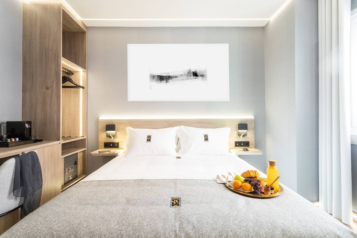 A hotel room with a bed, bedside tables, a desk, a wardrobe, and a breakfast tray with fruits and juice.