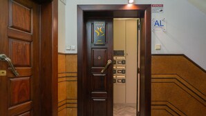 Entrada de hotel com porta de madeira, uma placa acima e um elevador com botões numerados.