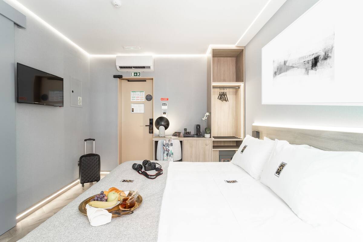 A hotel room with a bed, a desk, a chair, a television, and a wall-mounted air conditioner.
