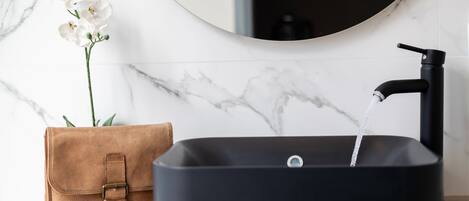 A black sink with a faucet, a brown leather bag, and a white orchid.