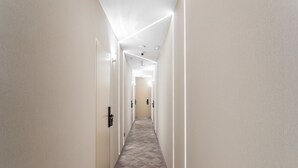 Um corredor estreito, bem iluminado, com piso em padrão herringbone e paredes brancas.