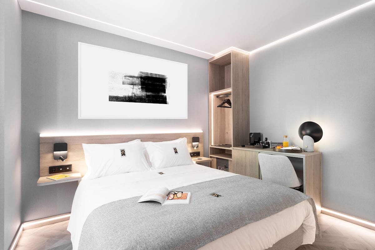 A modern hotel room with a neatly made bed, a desk, and a wardrobe.