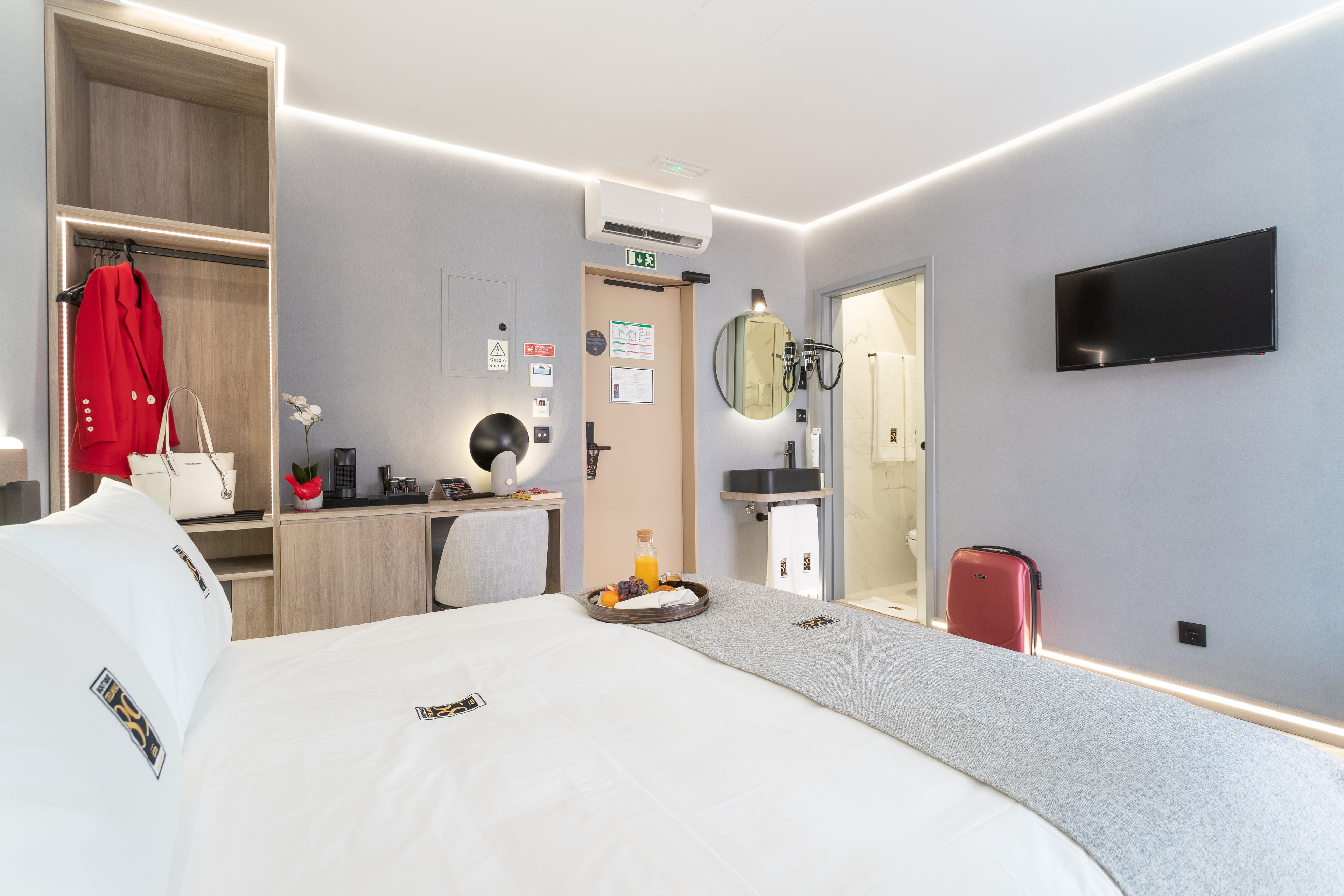 Una habitación de hotel con una cama, un escritorio, un espejo, un televisor y un armario.