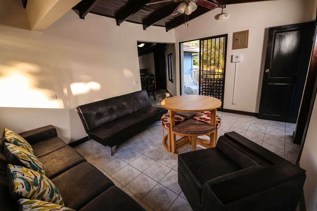 A living room with a black leather sofa, a round wooden table with chairs, and a black armchair.