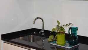 A kitchen sink with a modern faucet, a green plant in a yellow pot, and a teal pitcher on the countertop.