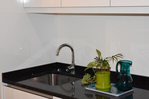 Enjoy cooking in this well-equipped kitchen with a stainless steel sink, white cabinets, and a black countertop.