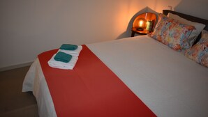 A neatly made bed with a red and white bedspread, two teal towels, and colorful patterned pillows.