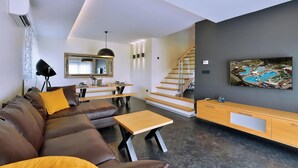 Een moderne woonkamer met een bruine leren bank, een eettafel en een trap naar een hoger niveau.