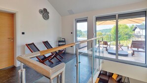 Ruime kamer met glazen balustrade, houten deur en uitzicht op een terras met zitplaatsen.