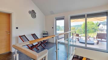 Ein geräumiger Raum mit Glastrennwand, Holztür und Blick auf eine Außenveranda mit Sitzgelegenheiten.