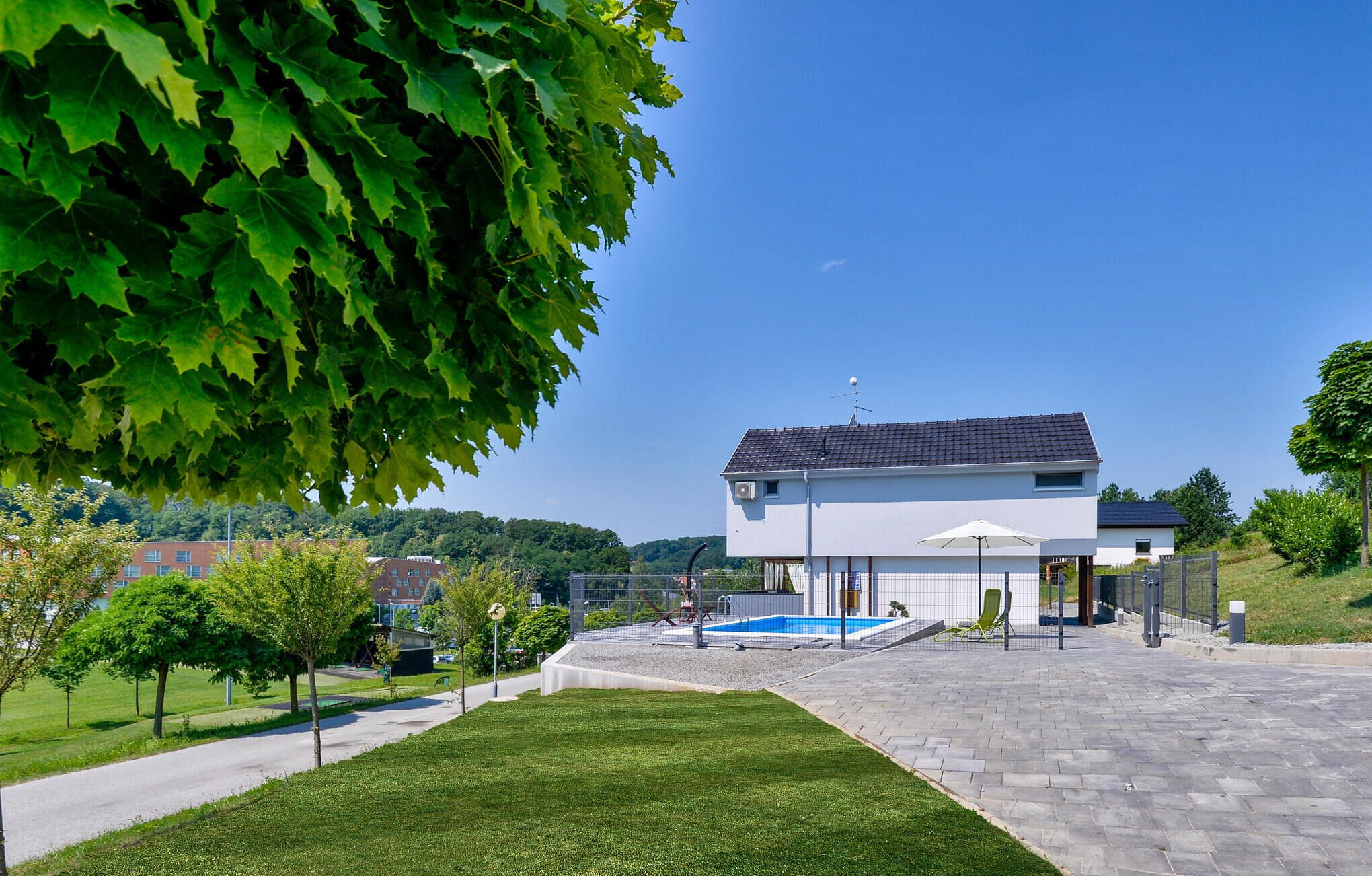 Ein modernes, zweistöckiges Haus mit Schwimmbecken, umgeben von einem gepflegten Rasen und Bäumen.