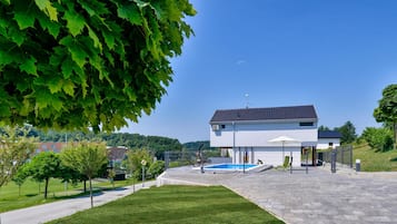 Ein modernes, zweistöckiges Haus mit Schwimmbecken, umgeben von einem gepflegten Rasen und Bäumen.