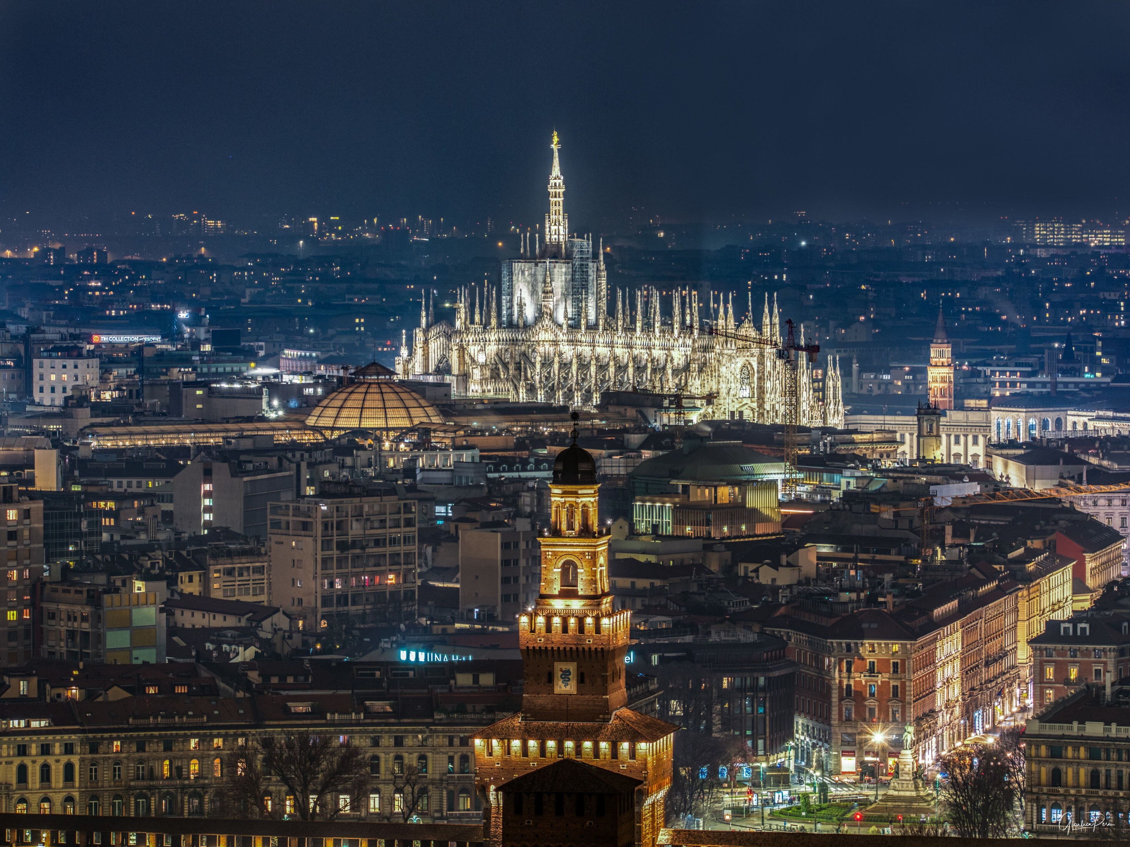 Paesaggio urbano notturno con edifici illuminati e una cattedrale in evidenza sullo sfondo.