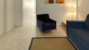 Een woonkamer met een blauwe bank, een donkere fauteuil, een vloerkleed en abstracte decoratie aan de muur.